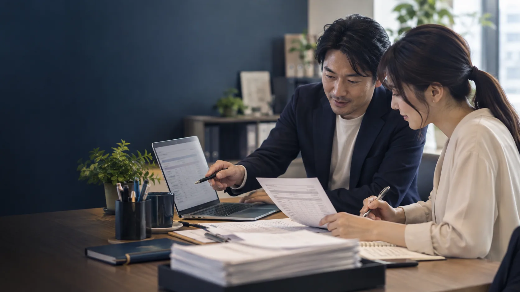 紙の書類とパソコンを見ながら、二人で作業を整理するイメージ